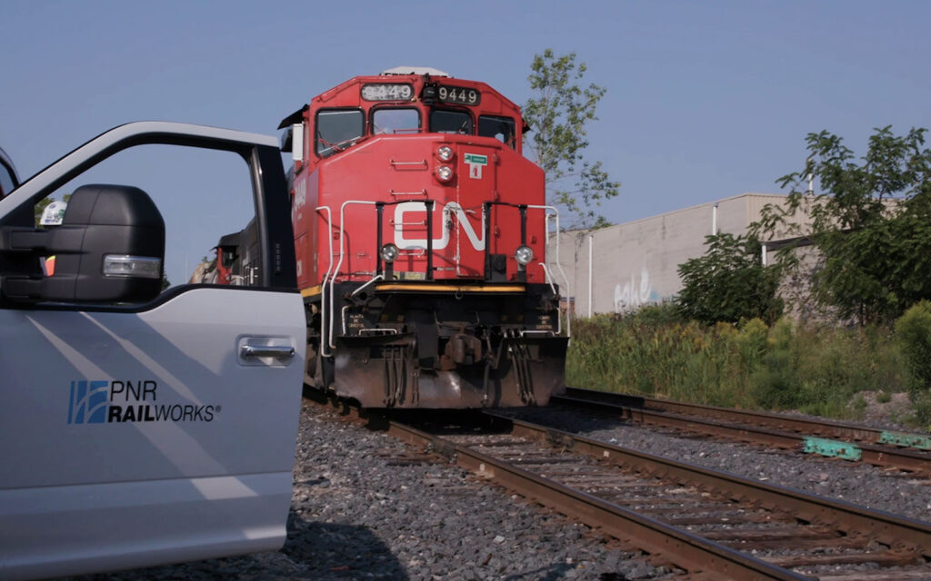 A medium shot photo of a inboard CN train with an open door of a RailWorks employee vehicle to the left.